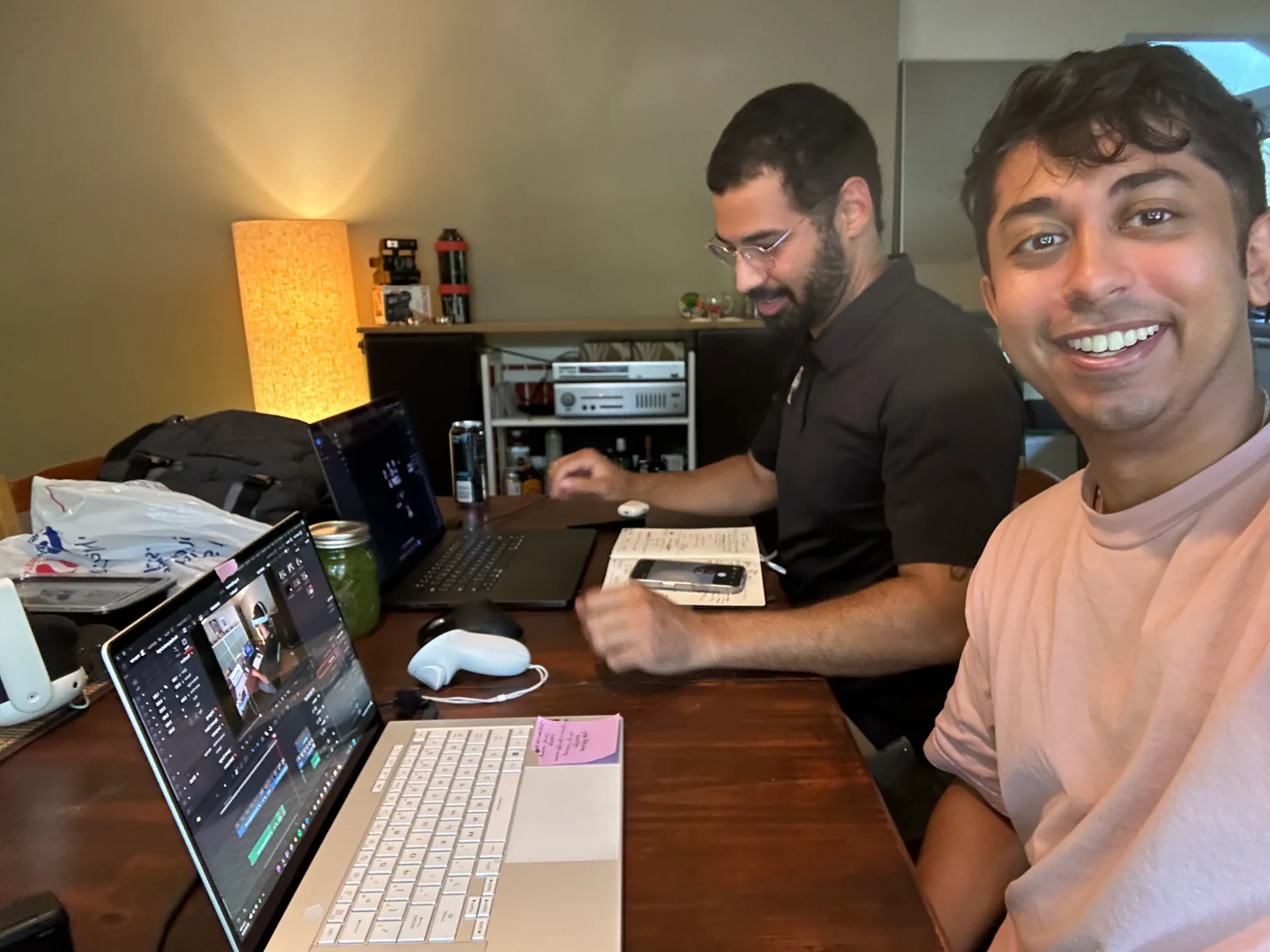 Selfie of Sid grinning beside Morgan, who works at a desk with laptops and a Quest controller during the hackathon