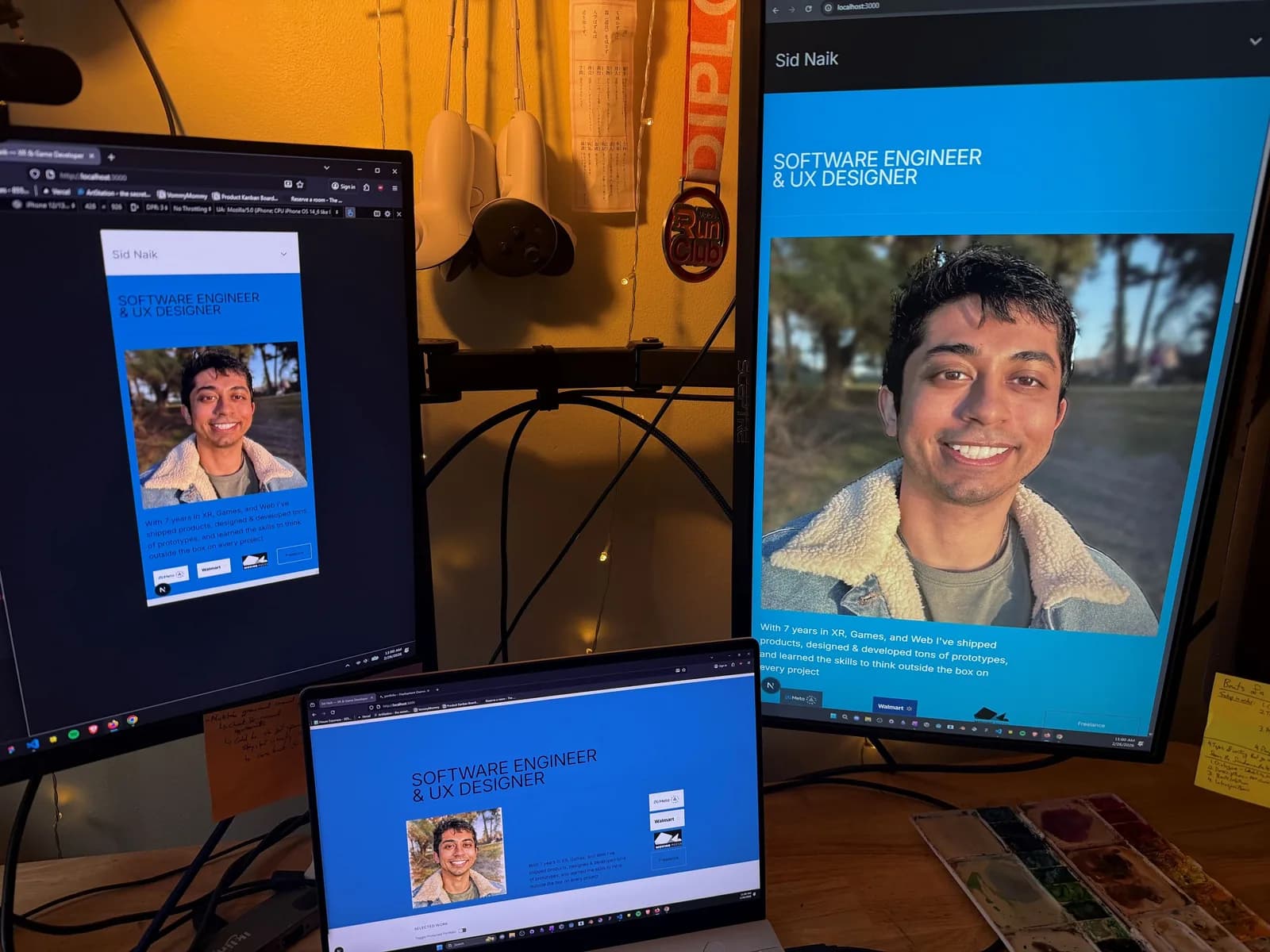 Three screens on a desk showing the new portfolio landing page — bright blue “Software Engineer & UX Designer” header with a portrait — at phone, desktop and laptop sizes